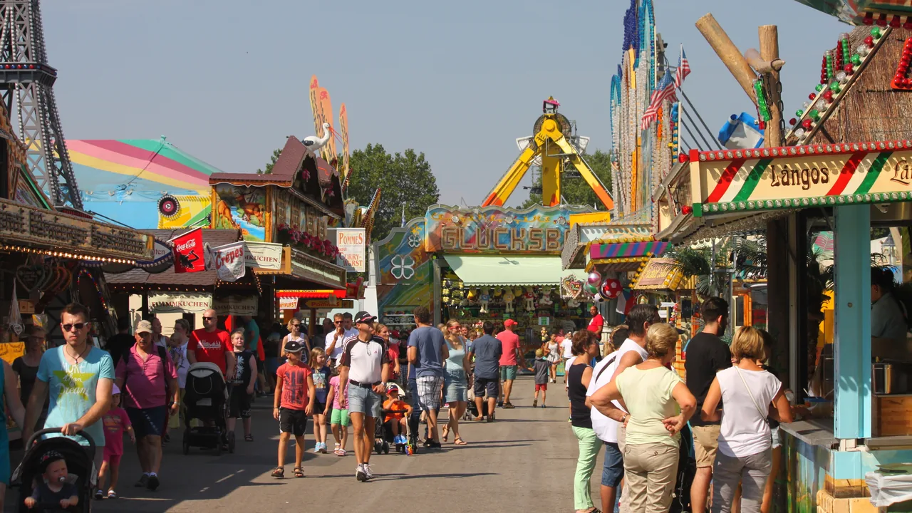Besucherinnen und Besucher auf der Festmeile des Nürnberger Volksfests am Dutzendteich, zwischen Imbissständen und Fahrgeschäften