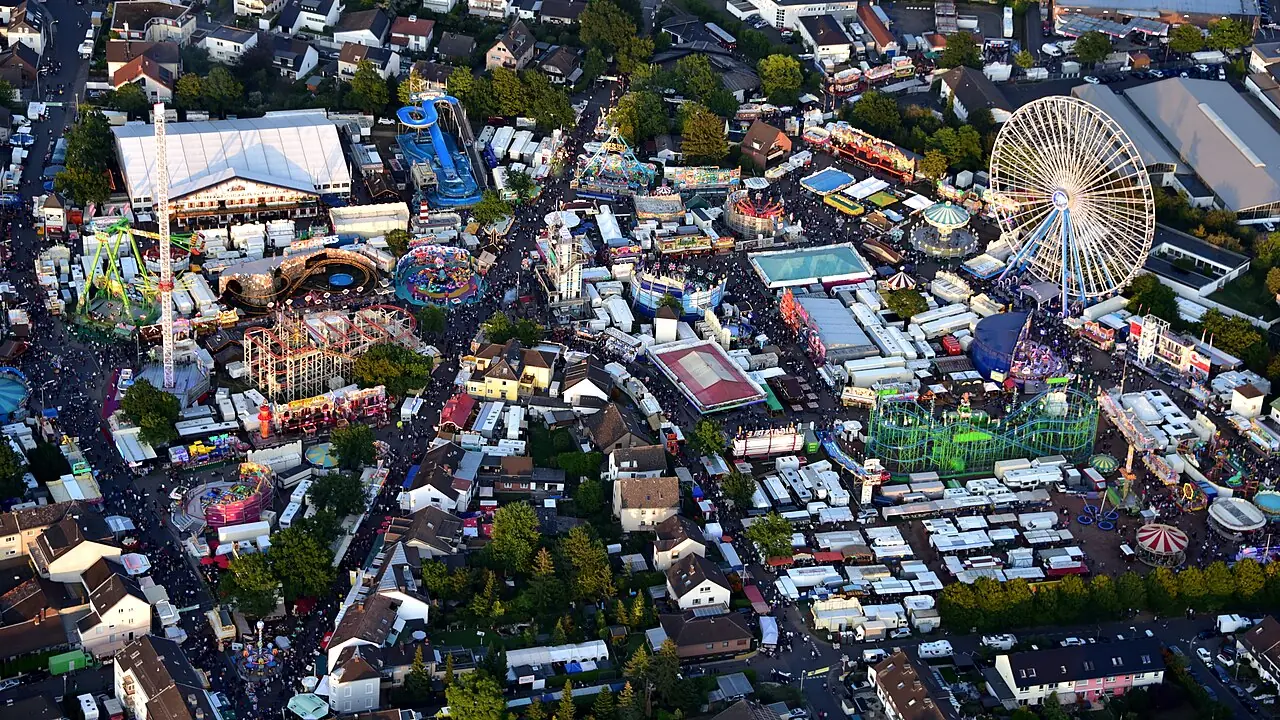 Luftaufnahme des Pützchens Markts in Bonn-Beuel am Abend: Riesenrad, Kettenkarussell, Achterbahnen und Budengassen zwischen Wohnhäusern