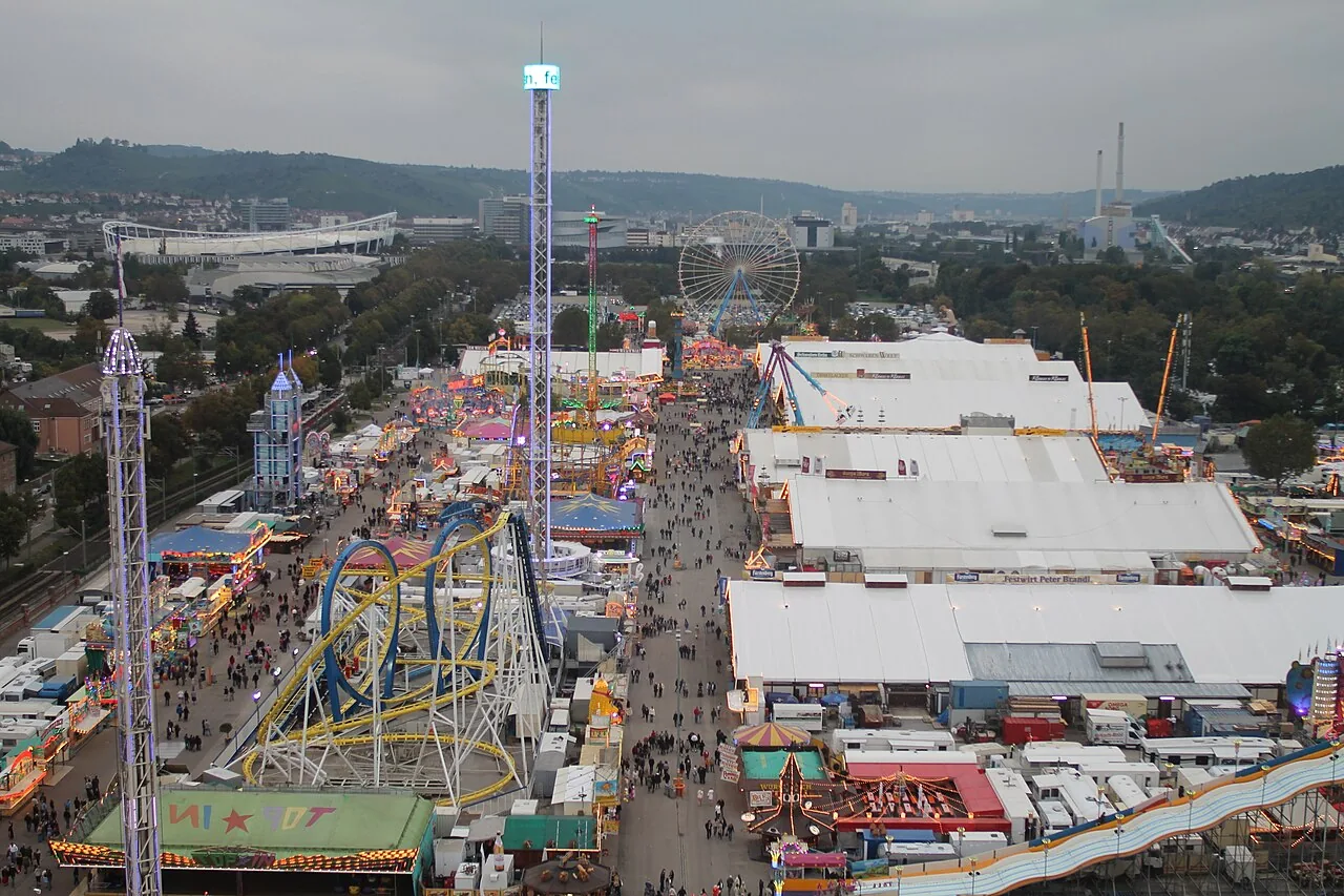 Blick vom Riesenrad über das Cannstatter Volksfest in Stuttgart: Festzelte, Achterbahn, Kettenflieger und die Budengasse, im Hintergrund das Neckarstadion