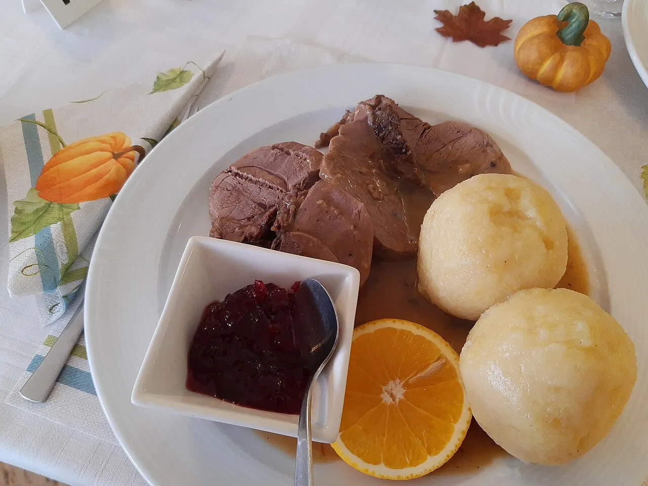 Teller mit Scheiben von geschmorter Rehkeule in Soße, zwei Kartoffelklößen, einer halben Orange und einem Schälchen Preiselbeeren, serviert im Gasthaus zum Taunus in Steckenroth