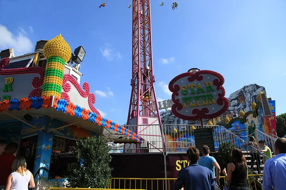 Buntes Fahrgeschäft und der Kettenflieger Star Flyer auf der Cranger Kirmes in Herne vor blauem Himmel