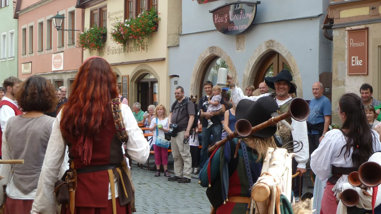 Spielleute in historischer Gewandung mit langen Holzhörnern ziehen bei den Reichsstadt-Festtagen durch eine Gasse der Rothenburger Altstadt, Zuschauer säumen die Fachwerkhäuser