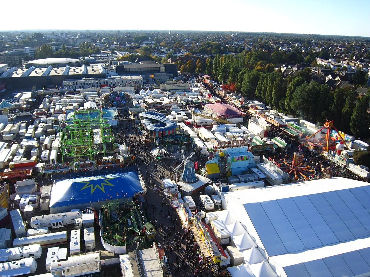 Blick vom Riesenrad über den Oldenburger Kramermarkt: Fahrgeschäfte, Buden und Festzelte an den Weser-Ems-Hallen, dahinter die Stadt Oldenburg
